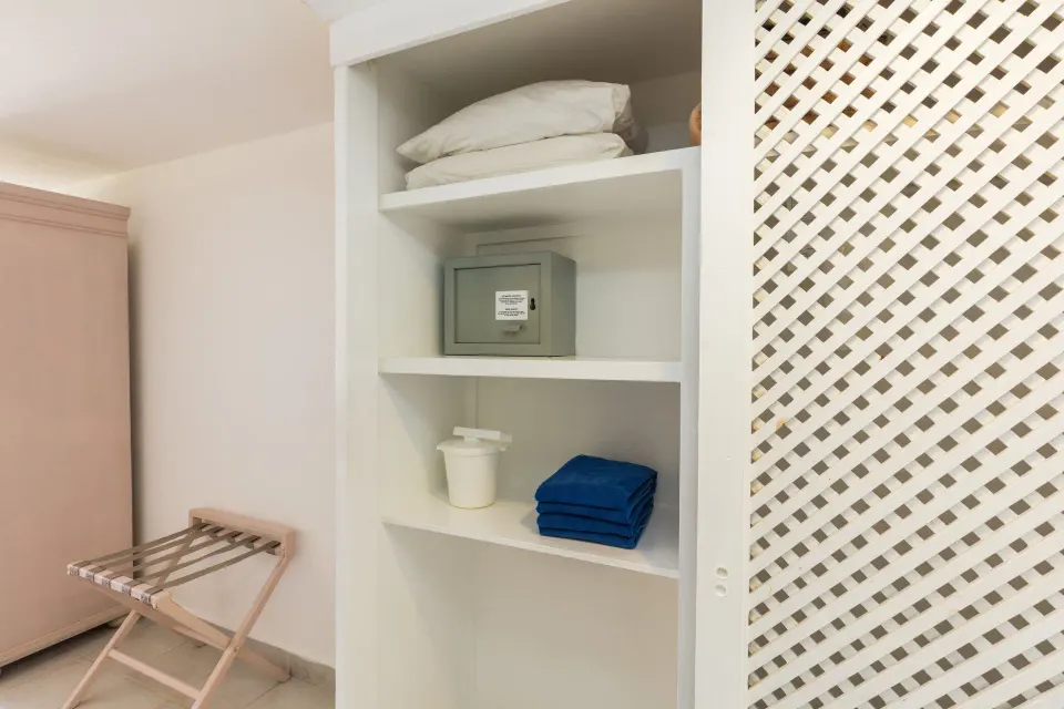 Open wardrobe shelves with safe and folded linens in a standard room at Posada Real Los Cabos.
