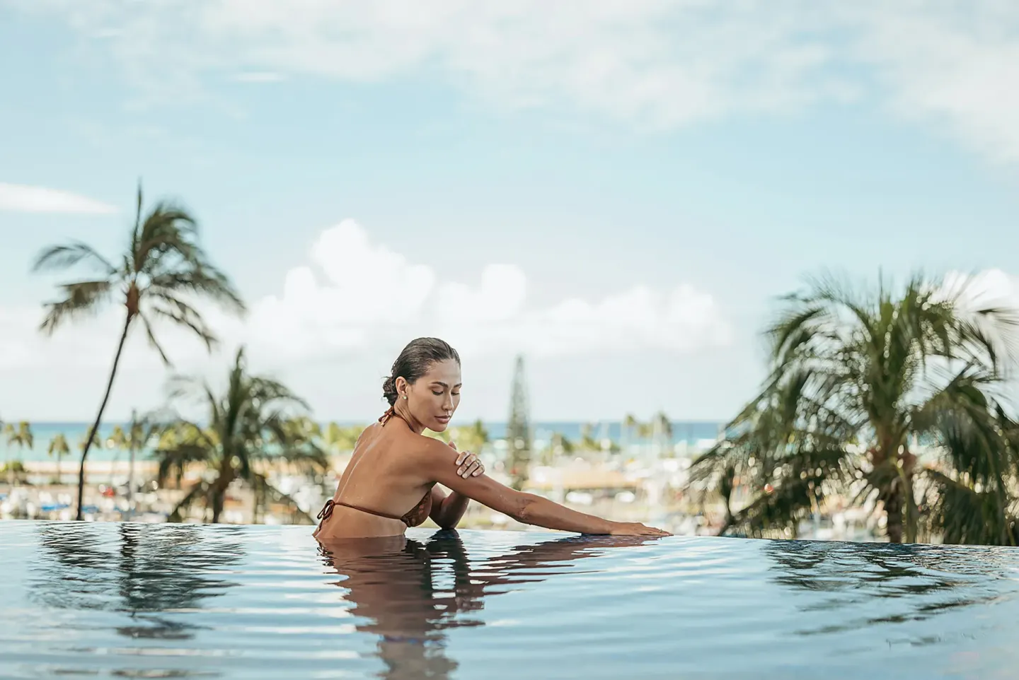 Guest leaning in the infinity pool with palm trees and ocean beyond at Prince Waikiki.
