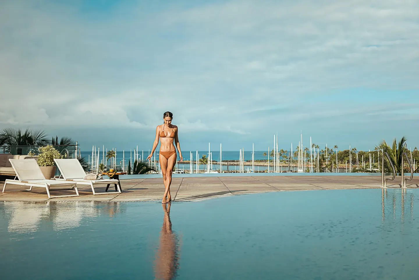 Guest walking by the pool with marina masts and ocean beyond at Prince Waikiki.