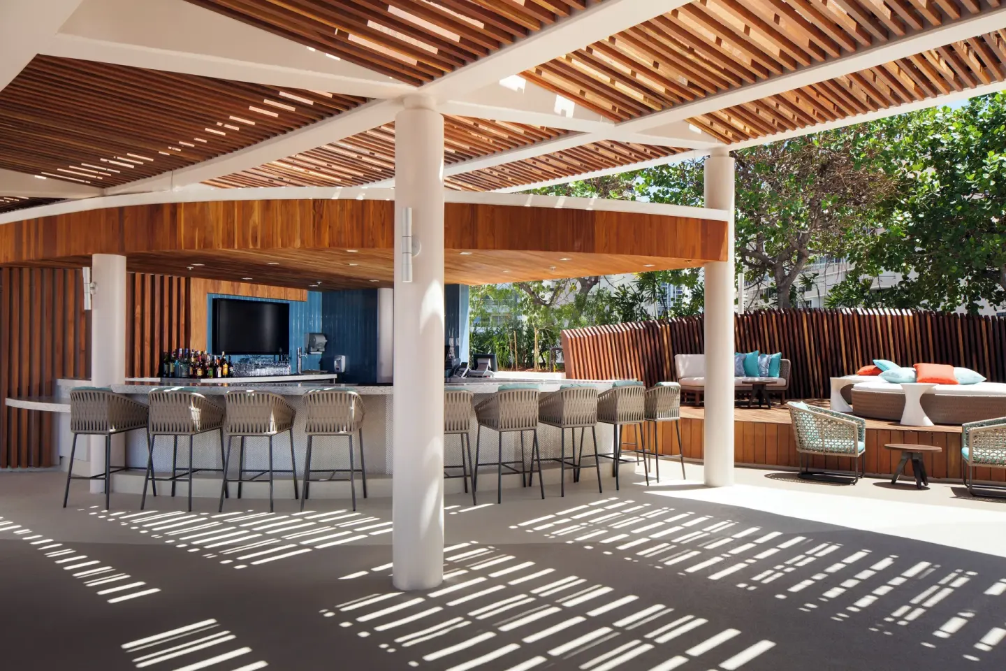 Poolside bar with stools, wood slat ceilings, and lounge seating at Prince Waikiki.