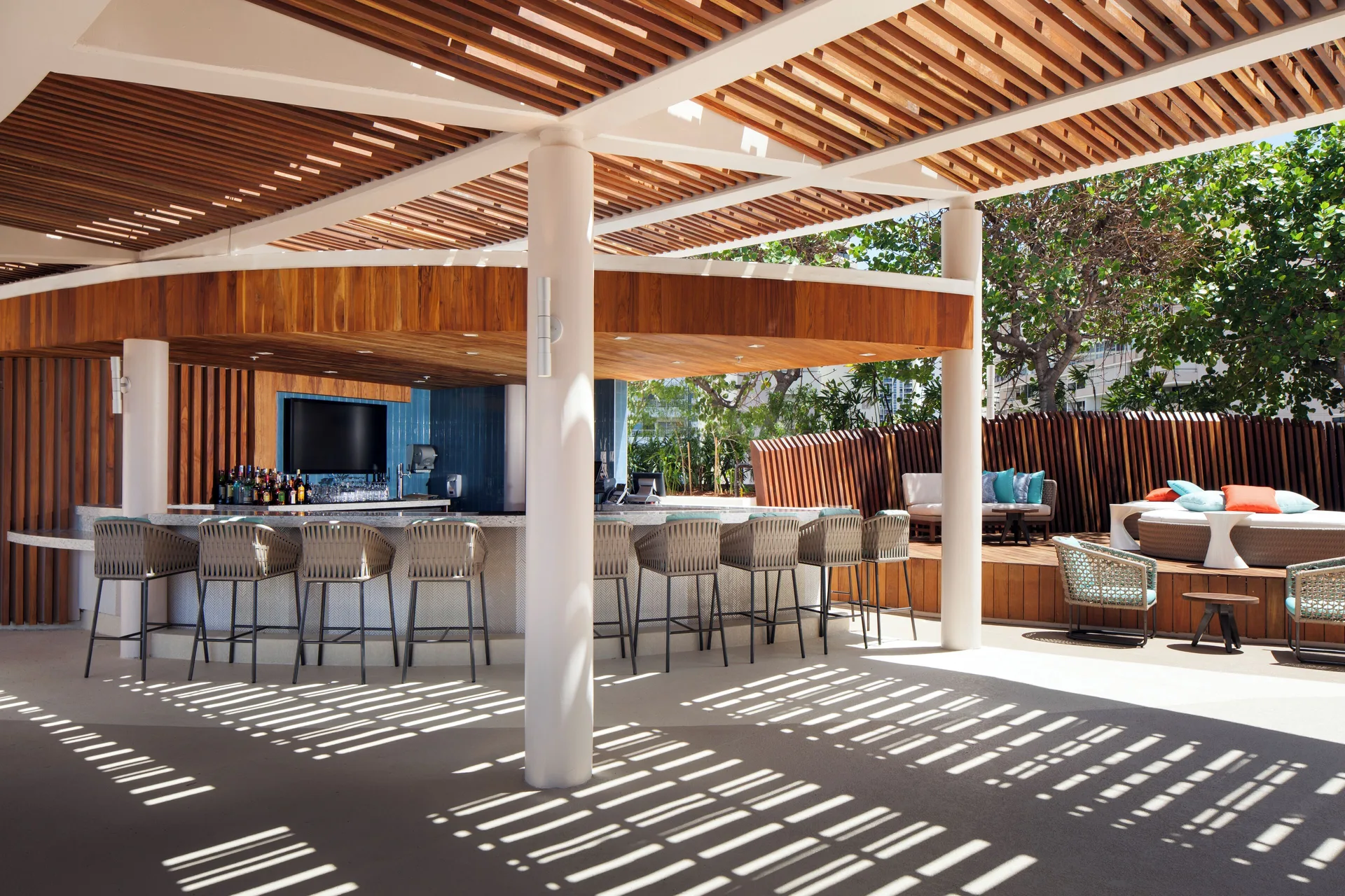 Poolside bar with stools, wood slat ceilings, and lounge seating at Prince Waikiki.