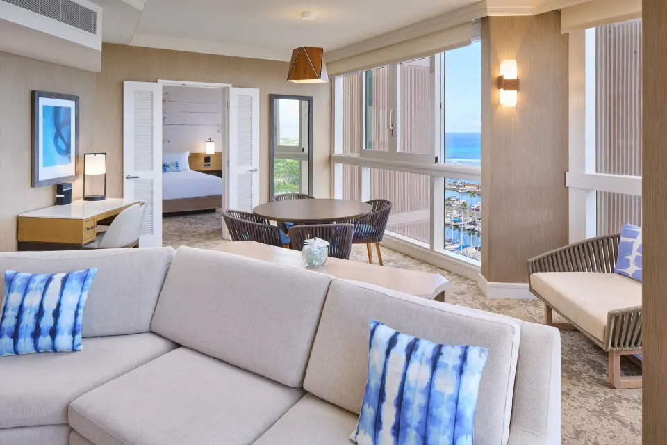 Ocean Front 1 Bedroom Suite living room with sofa, dining table, and bedroom doorway at Prince Waikiki.
