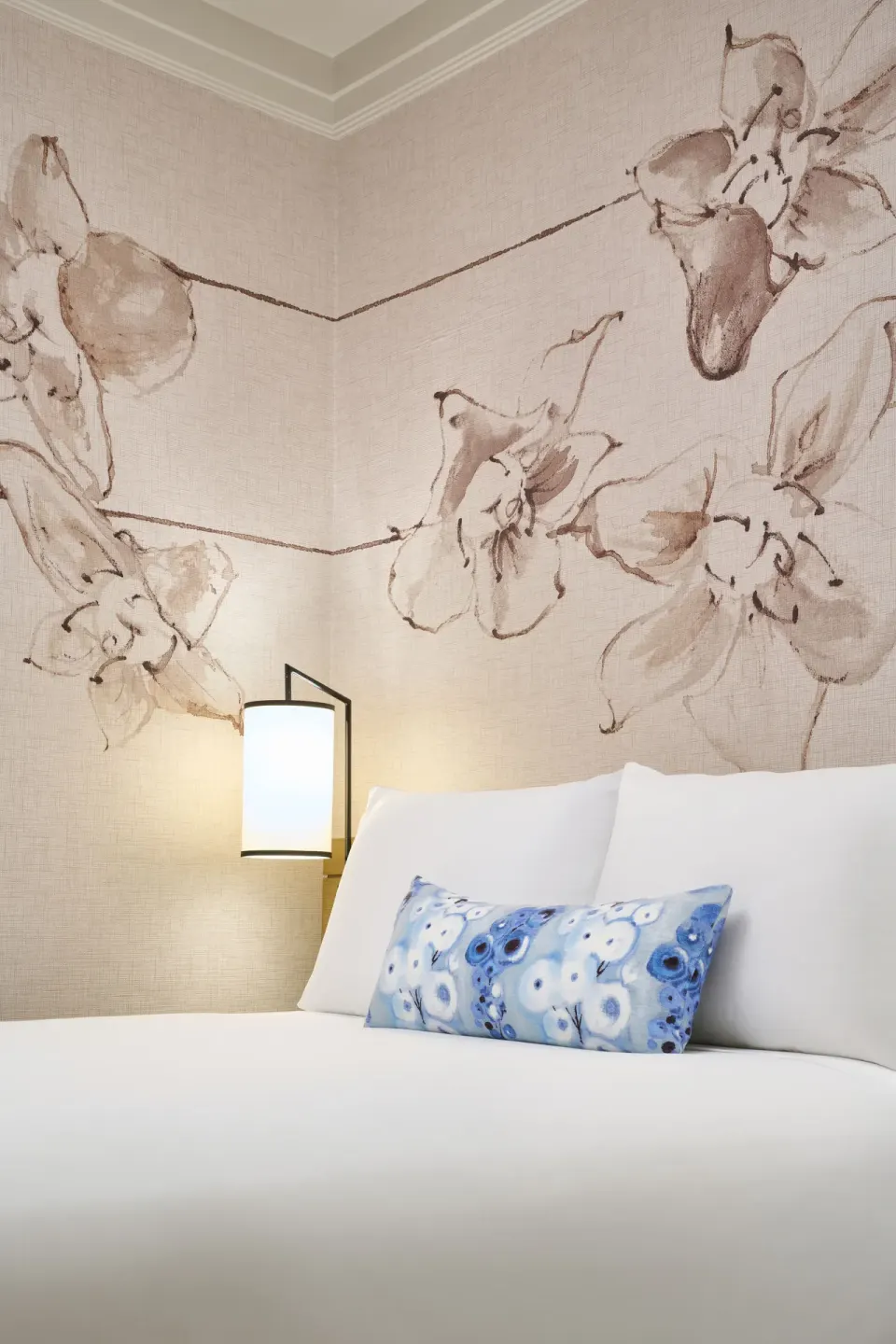 Ocean Front Harbor bed detail at Prince Waikiki with white pillows, blue accent pillow, lamp, and floral wall art.