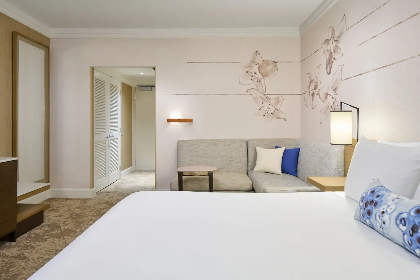 Ocean Front Harbor king room at Prince Waikiki with bed, corner sofa, hallway, and floral wall mural.