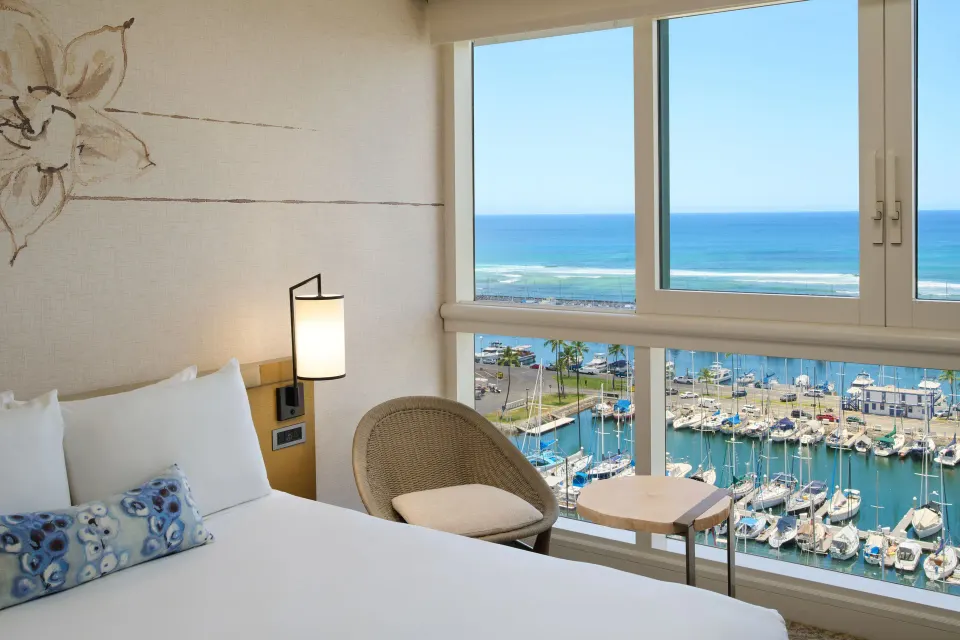 Ocean Front Harbor room at Prince Waikiki with bed corner, chair, table, and marina and ocean view.