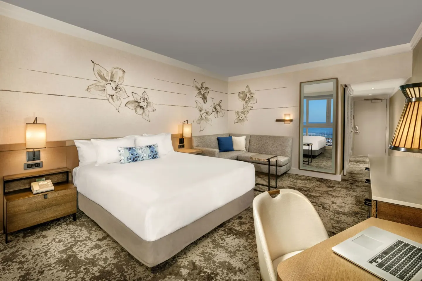 Ocean Front Harbor king room at Prince Waikiki with bed, sofa, desk, and mirror reflecting the ocean view.