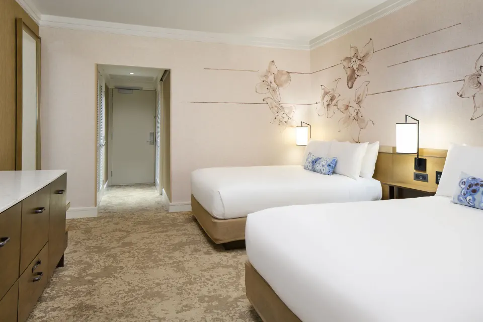 Ocean Front Harbor room at Prince Waikiki with two beds, bedside lamps, floral wall art, and entry hallway.