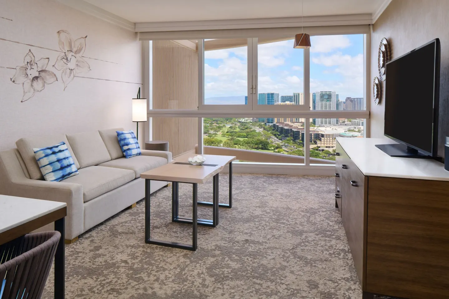 Ocean View Suite living room with sofa, TV, and skyline windows at Prince Waikiki.
