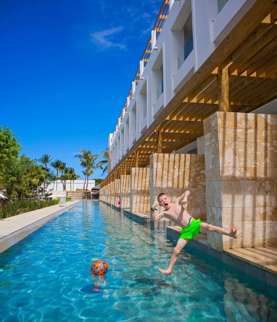 Child jumping beside a swim-up pool outside guest buildings at Princess Family Club Bavaro.