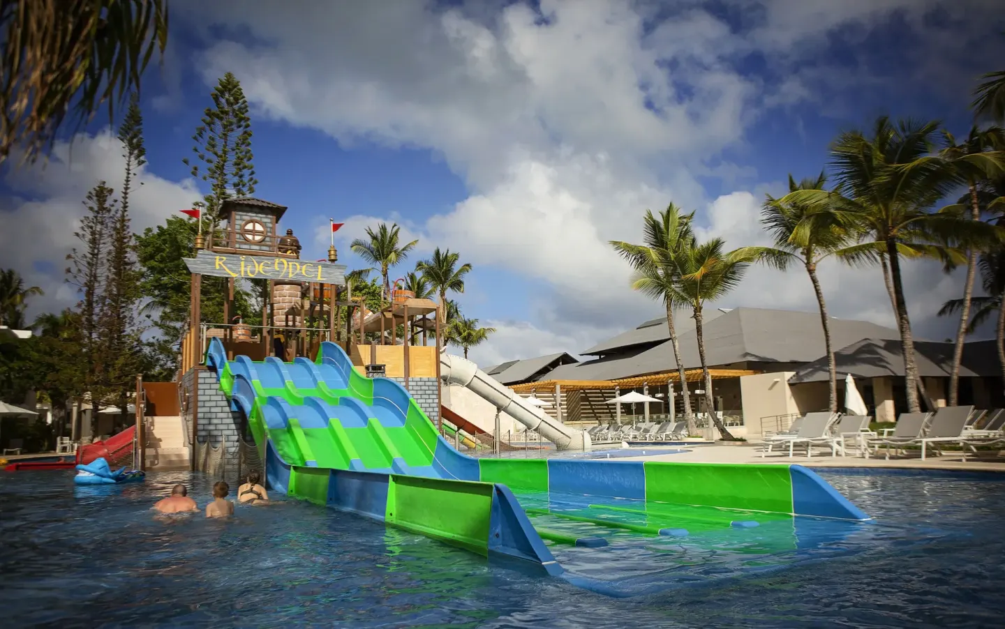 Guests in the pool near a green and blue water slide at Princess Family Club Bavaro.