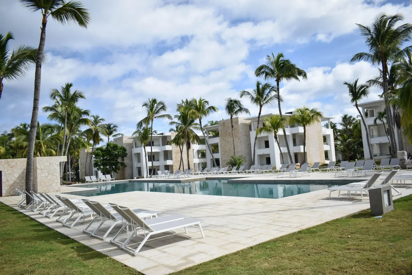 Open pool deck with lounge chairs, palms, and white buildings at Princess Family Club Bavaro.