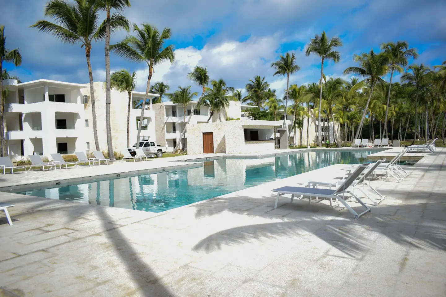 Rectangular pool with white loungers and palm-lined room buildings at Princess Family Club Bavaro.