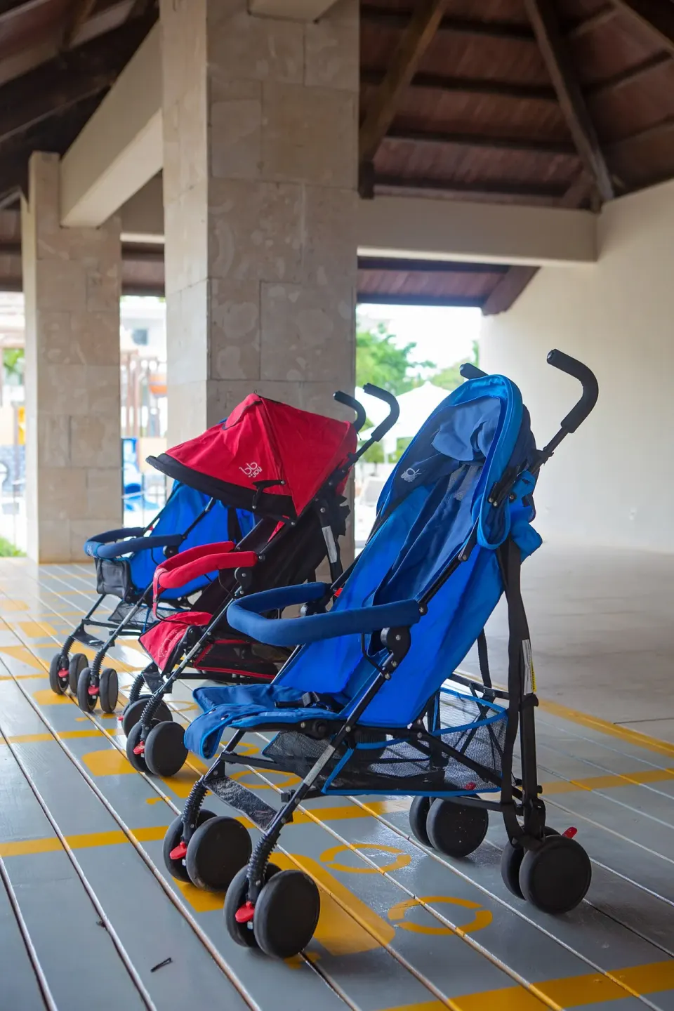 Blue and red strollers lined up under a covered walkway at Princess Family Club Bavaro.