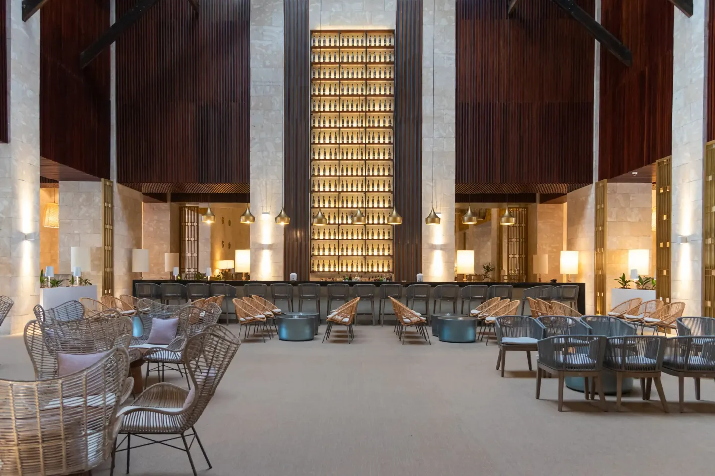 Tall lobby bar with woven chairs and a backlit bottle display at Princess Family Club Bavaro.