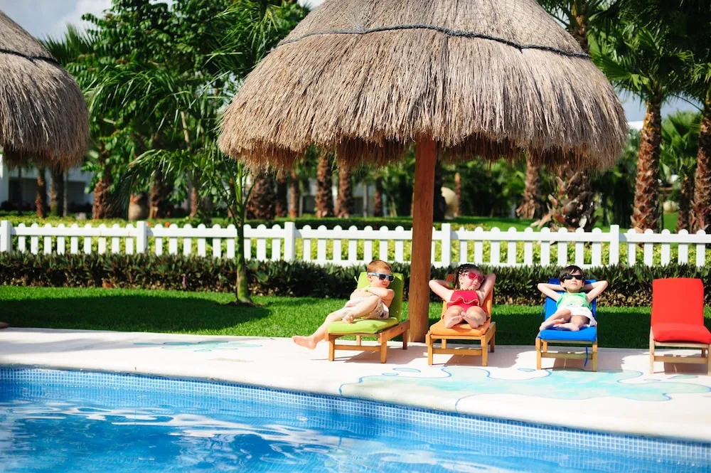 Children relax on poolside loungers under thatched shade at Princess Family Club Riviera.