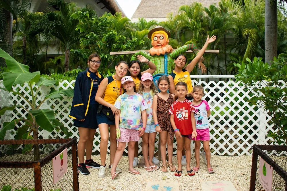 Children and staff pose in a tropical garden area at Princess Family Club Riviera.