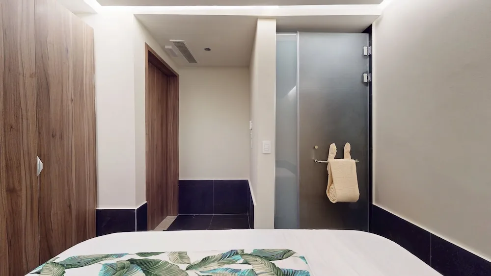 Guest room entry area with bed edge, wardrobe, and glass shower at Princess Grand Jamaica Resort.