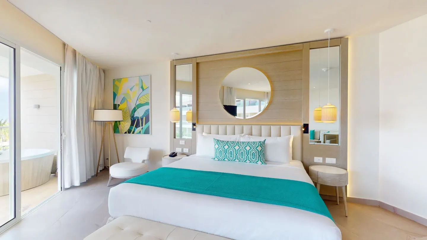 King bed guest room with balcony doors and tropical artwork at Princess Grand Jamaica Resort.