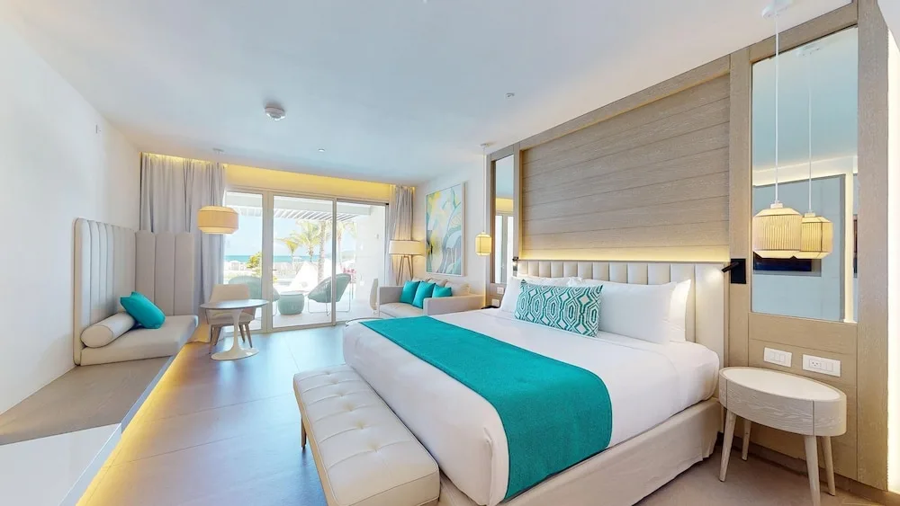 Guest room with king bed, bench, daybed, and balcony doors at Princess Grand Jamaica Resort.