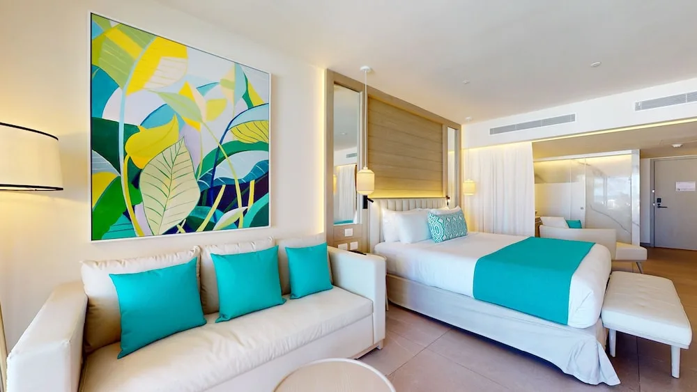Guest room with king bed, white sofa, and colorful leaf artwork at Princess Grand Jamaica Resort.