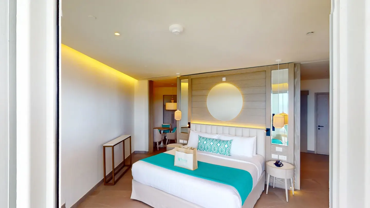 Guest room with king bed, round wall mirror and warm lighting at Princess Grand Jamaica Resort.