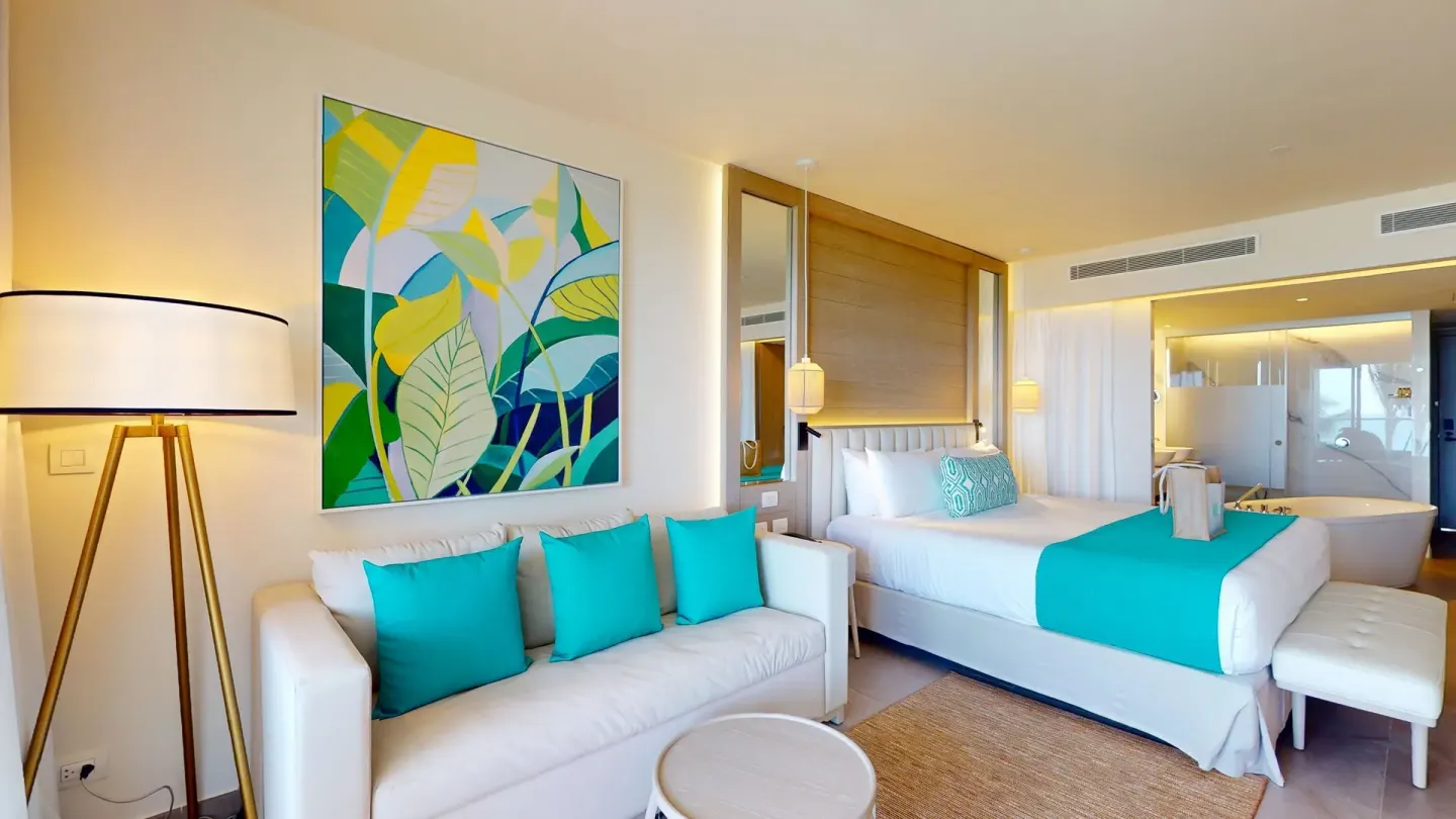 Guest room with king bed, sofa, artwork and open bath area at Princess Grand Jamaica Resort.
