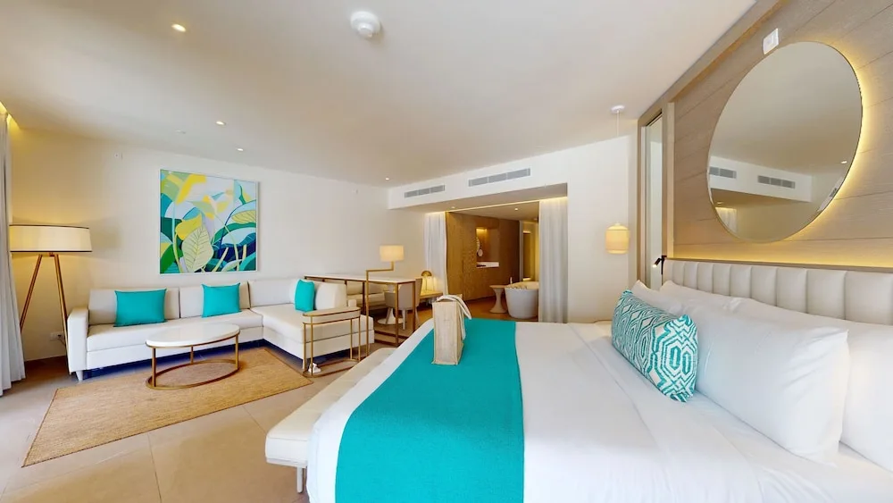 Guest room with king bed, sofa seating, and round mirror at Princess Grand Jamaica Resort.