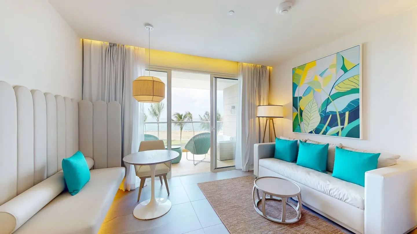 Guest room sitting area with sofa, dining nook and balcony at Princess Grand Jamaica Resort.