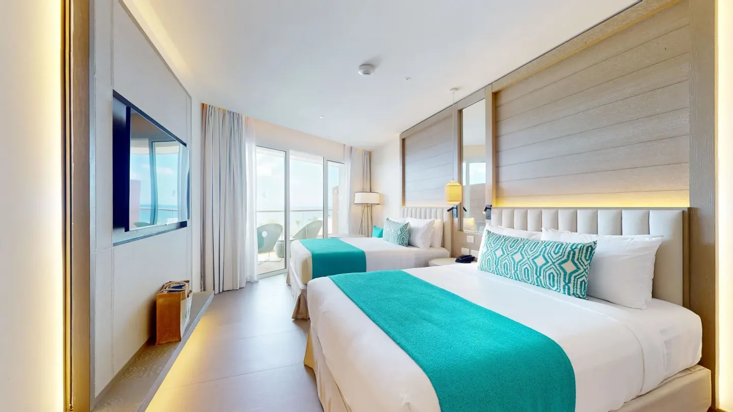 Guest room with two beds, turquoise accents and balcony doors at Princess Grand Jamaica Resort.