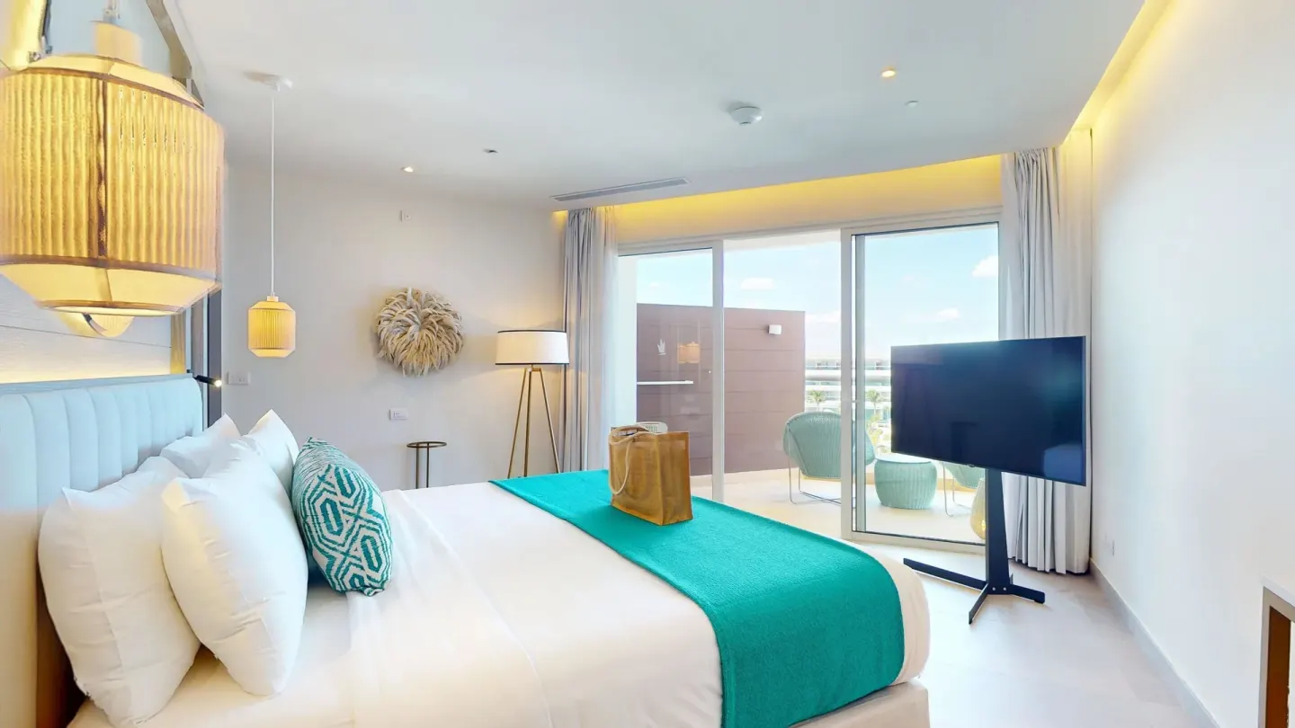 Imperial 1 Bedroom Master Suite bedroom with TV and balcony doors at Princess Grand Jamaica Resort.