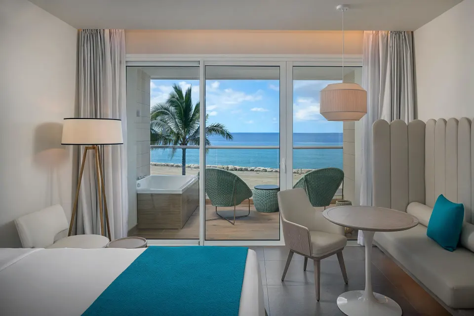 Platinum Junior Suite bed, seating area and ocean balcony at Princess Grand Jamaica Resort.