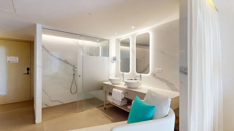 Princess Junior Suite bathroom at Princess Grand Jamaica Resort with glass shower, double sinks and lounge chair.