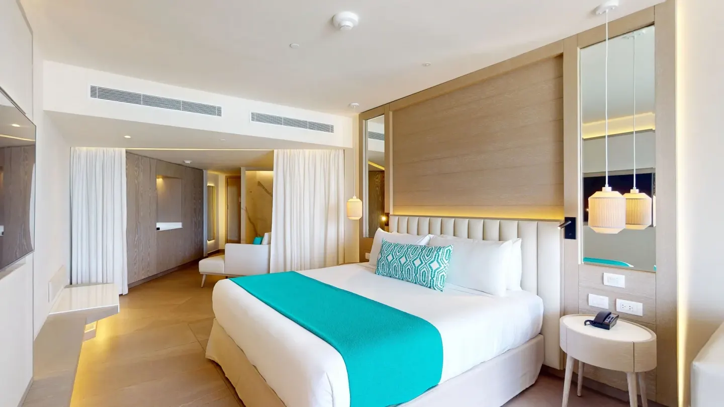 Princess Junior Suite at Princess Grand Jamaica Resort with king bed, bedside table and open sitting area.