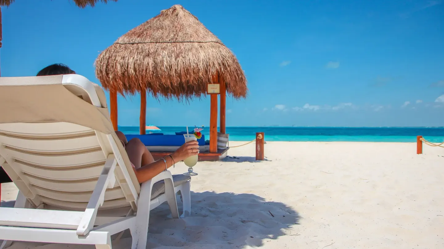 Beach lounger under a thatched shade facing the sea at Privilege Aluxes Isla Mujeres.
