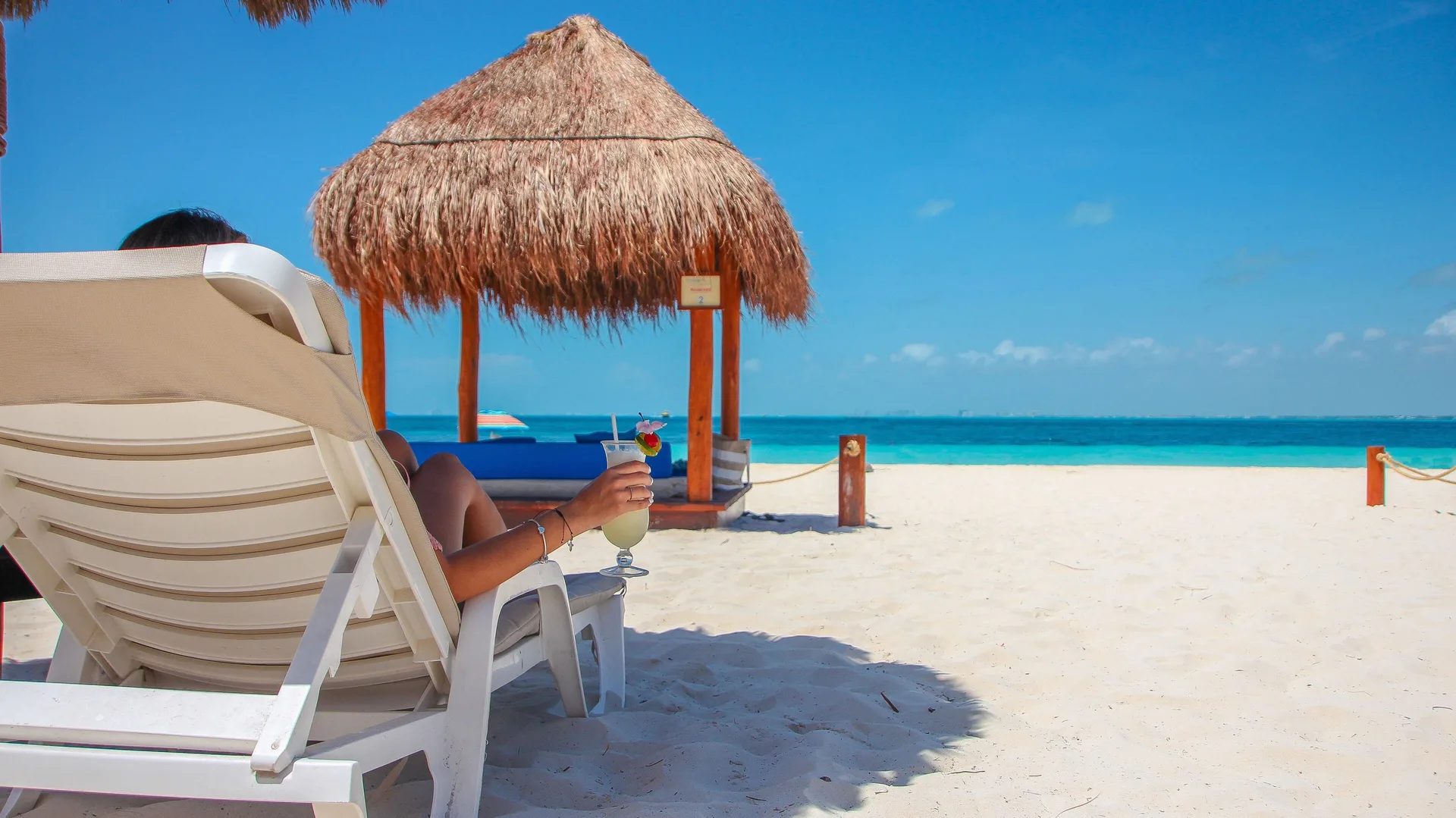 Beach lounger under a thatched shade facing the sea at Privilege Aluxes Isla Mujeres.