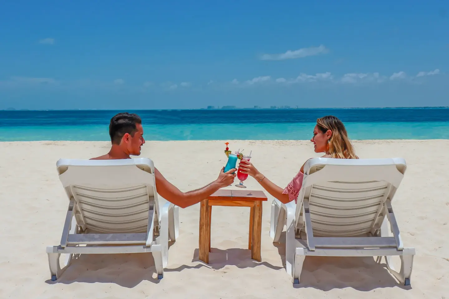 Two guests toast colorful drinks on beach loungers at Privilege Aluxes Isla Mujeres.