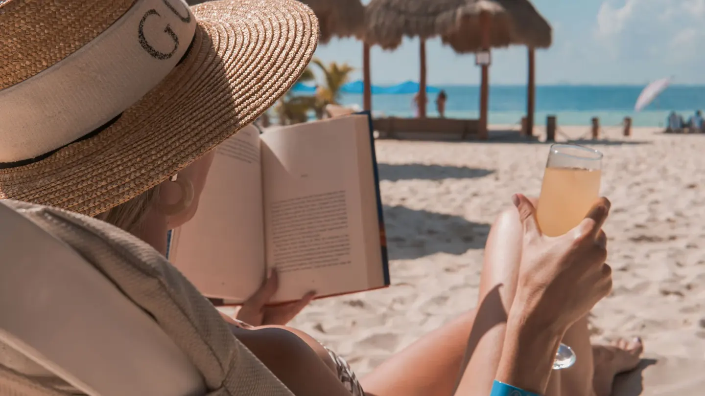 A guest reads with a drink on the beach at Privilege Aluxes Isla Mujeres.