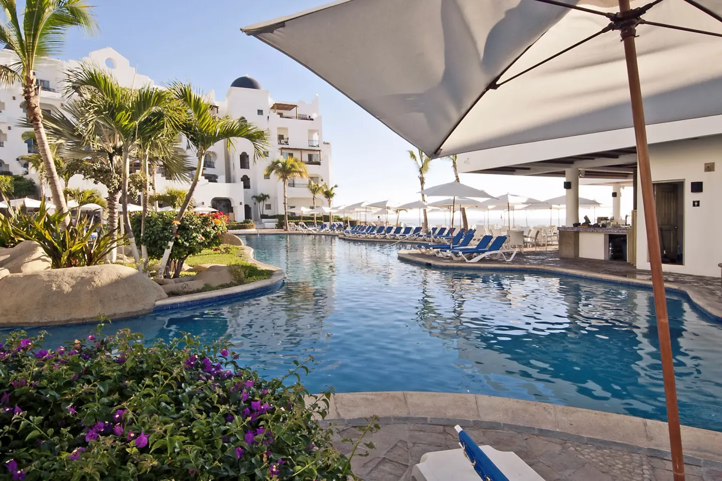 Curving pool with umbrellas, palms, and lounge chairs at Pueblo Bonito Los Cabos Blanco.