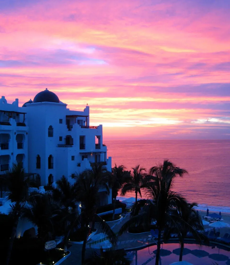 Resort building, palms, pool area, and ocean at sunset at Pueblo Bonito Los Cabos Blanco.