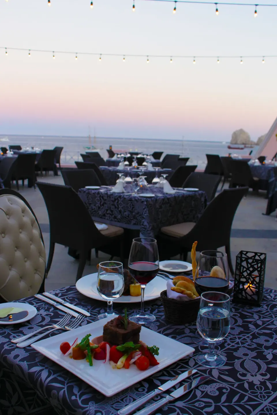 Outdoor dinner table with wine, bread, and an entrée by the sea at Pueblo Bonito Los Cabos Blanco.