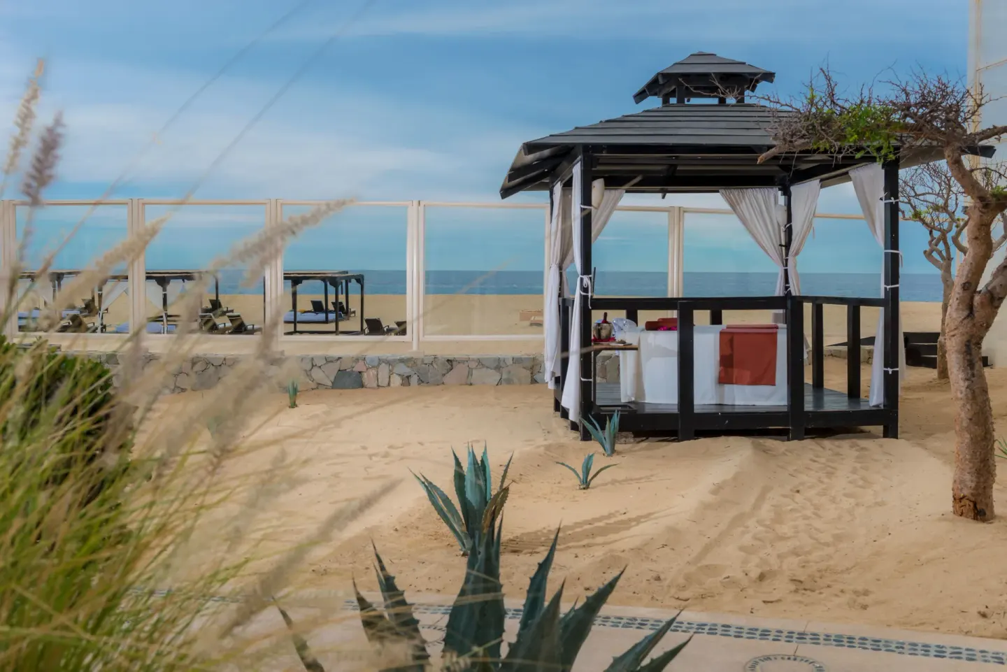Beachfront spa cabana with curtains and a treatment table on the sand at Pueblo Bonito Pacifica Golf & Spa Resort.