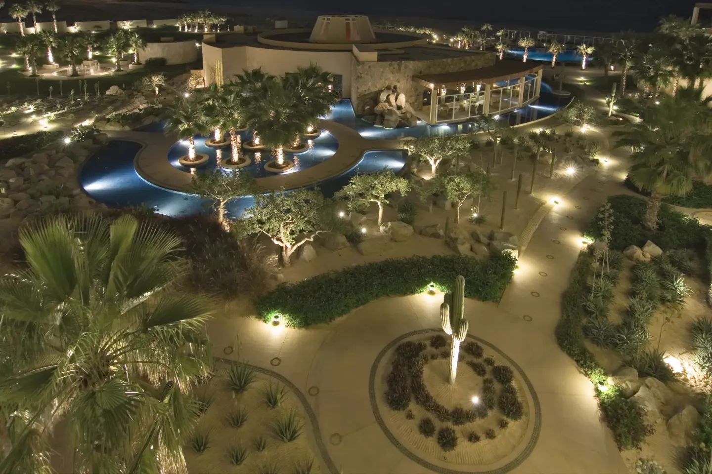 Illuminated pools, palms, and garden paths at night at Pueblo Bonito Pacifica Golf & Spa Resort.