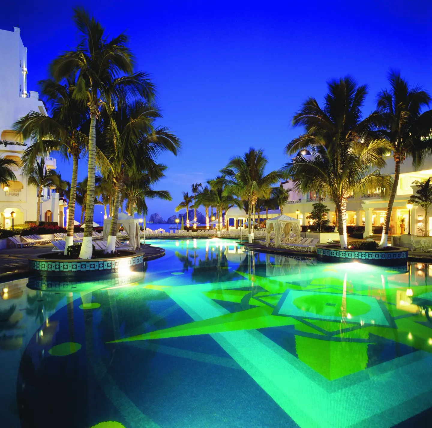 Blue-hour pool with glowing water, palm trees, and resort buildings at Pueblo Bonito Rose Resort and Spa.
