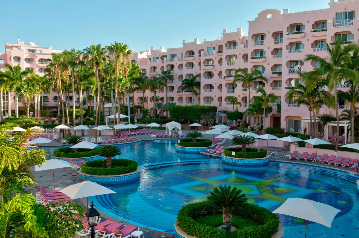 Courtyard pool with umbrellas, pink loungers, palms, and guest balconies at Pueblo Bonito Rose Resort and Spa.