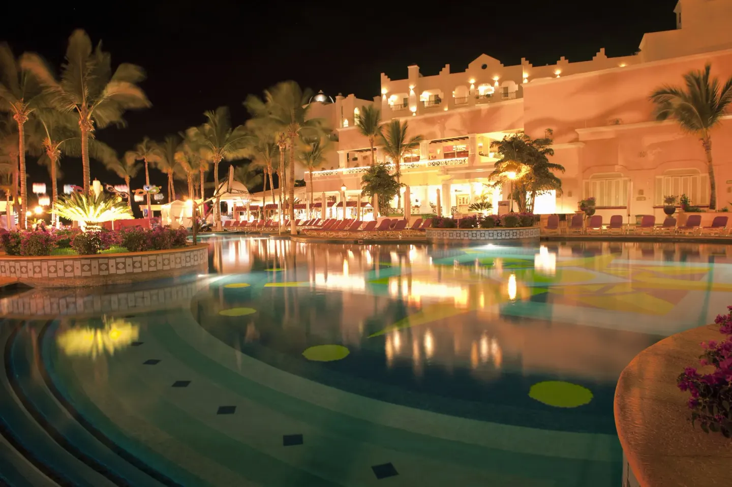 Night pool scene with palms, lounge chairs, and lit resort building at Pueblo Bonito Rose Resort and Spa.