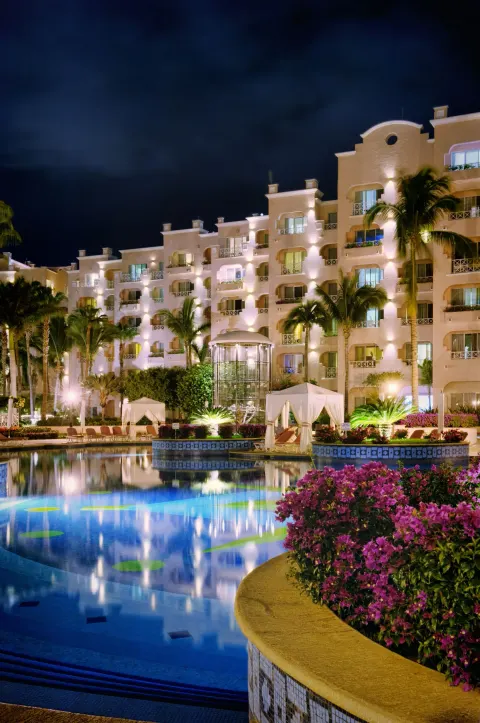 Nighttime pool, illuminated guest buildings, palms, and flowers at Pueblo Bonito Rose Resort and Spa.