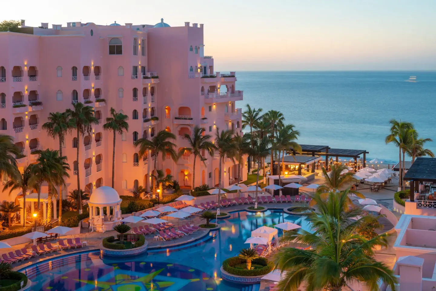 Resort pool, pink hotel buildings, palm trees, and ocean at Pueblo Bonito Rose Resort and Spa.