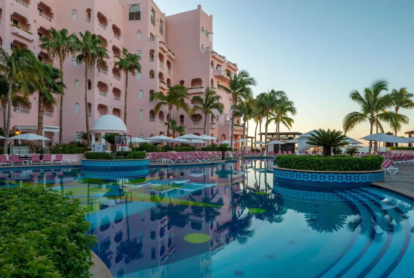 Pool with palm islands, lounge chairs, umbrellas, and pink buildings at Pueblo Bonito Rose Resort and Spa.