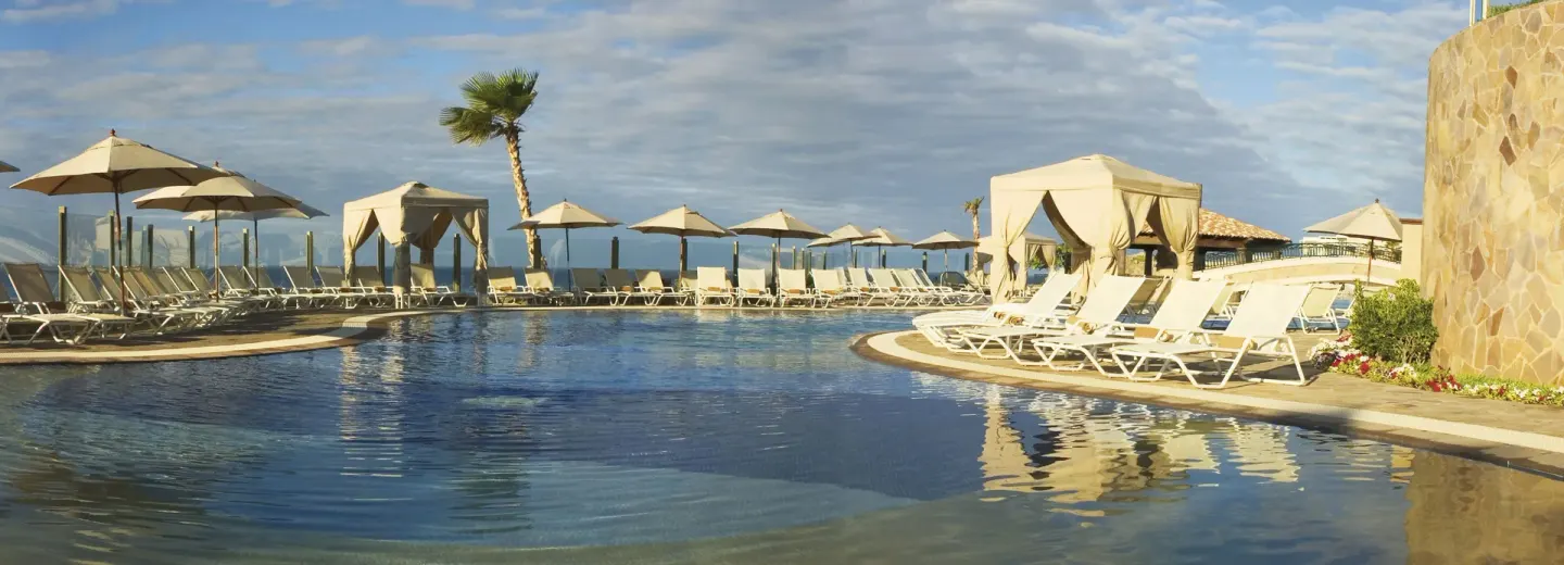 Curved pool with cabanas and ocean-edge loungers at Pueblo Bonito Sunset Beach Golf & Spa Resort.