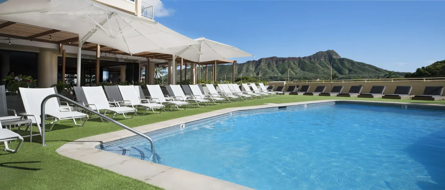 Curved pool edge with white loungers and Diamond Head at Queen Kapiolani Hotel.